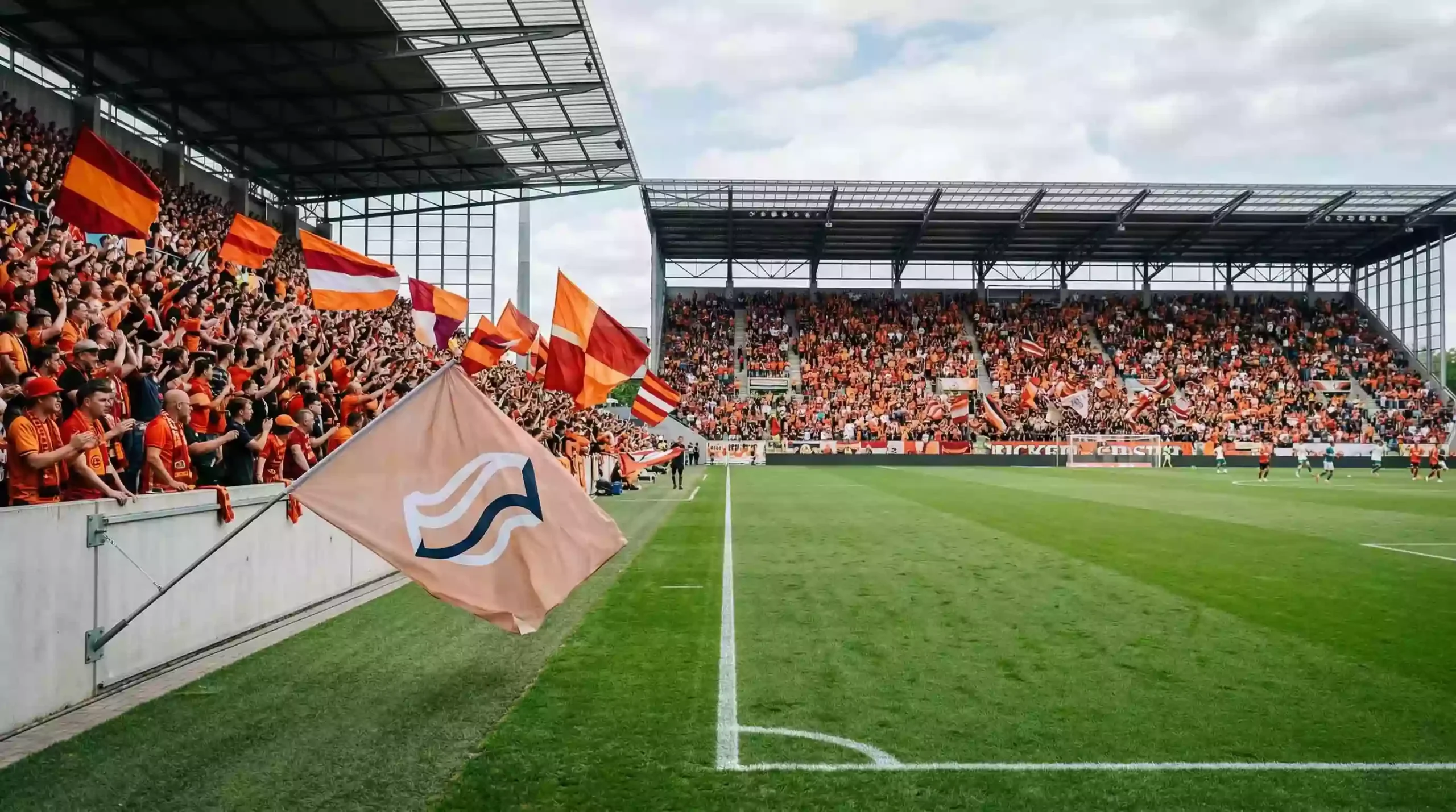 Estadio de fútbol japonés de segunda división con aficionados naranja celebrando un nuevo capítulo del club