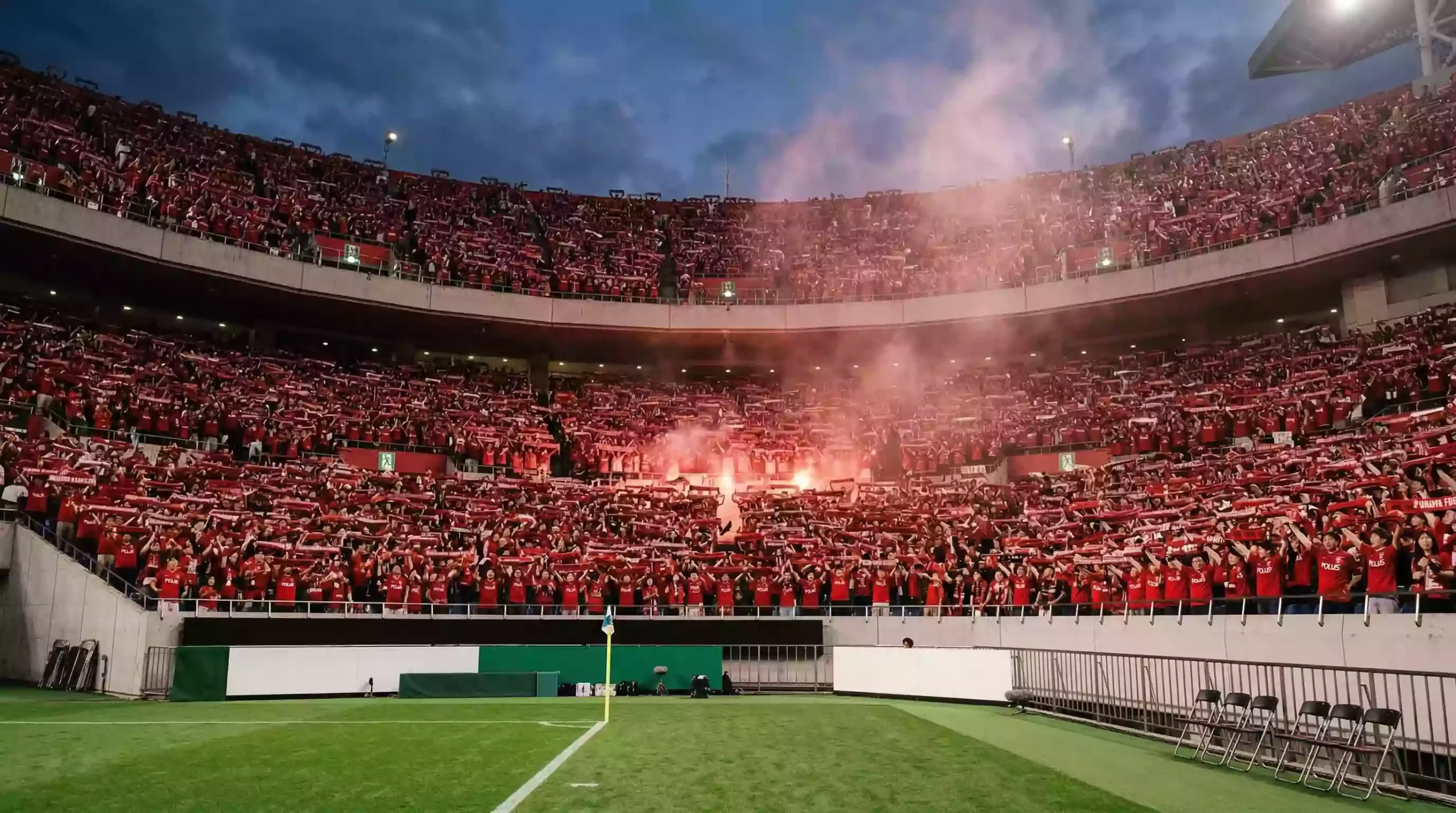 Tribuna llena del estadio de Urawa Red Diamonds con miles de aficionados con banderas rojas
